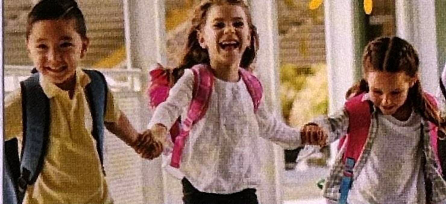Tres niños con mochila corriendo de la mano y riendo.